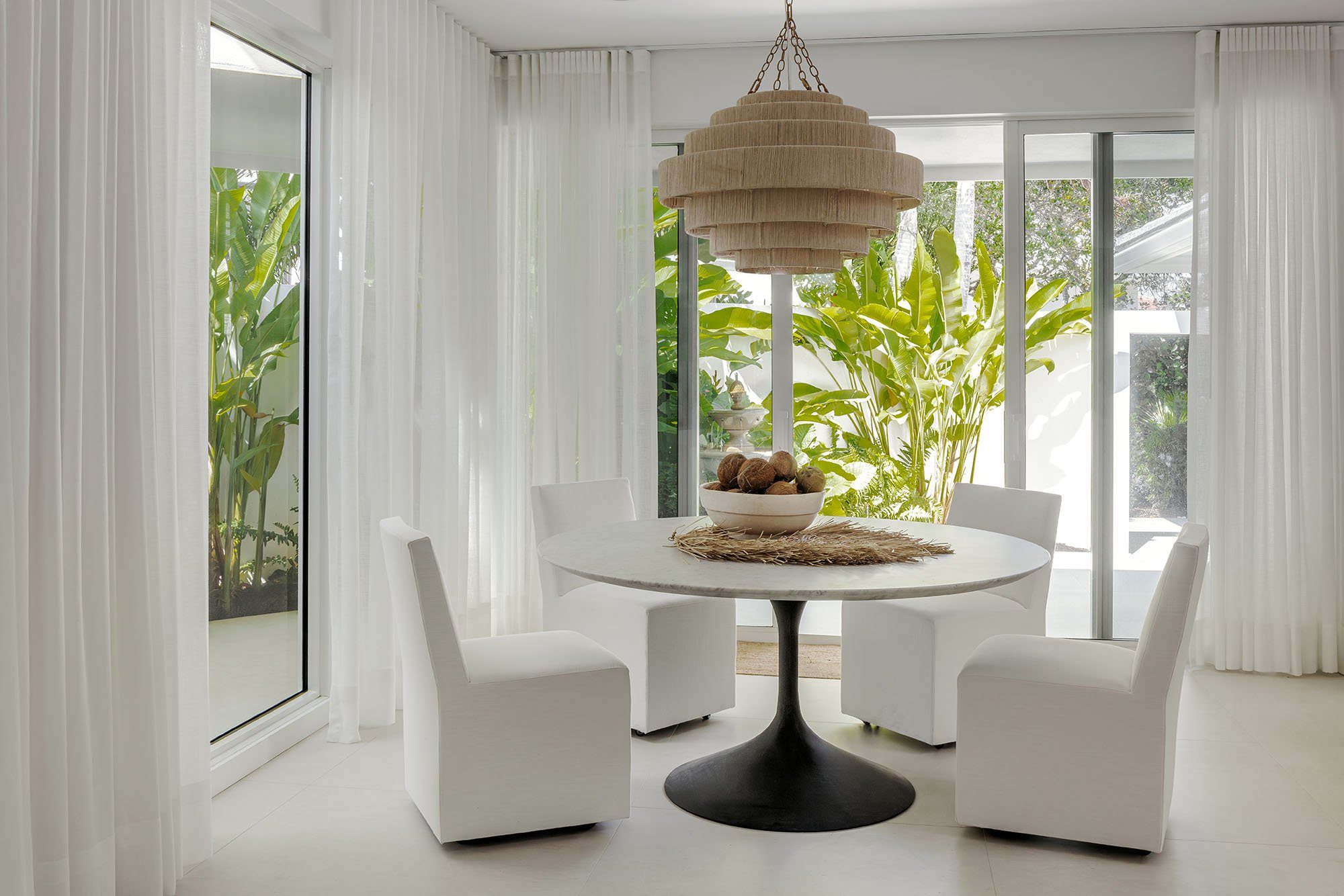 Bright white dining room with a woven chandelier and tropical garden view