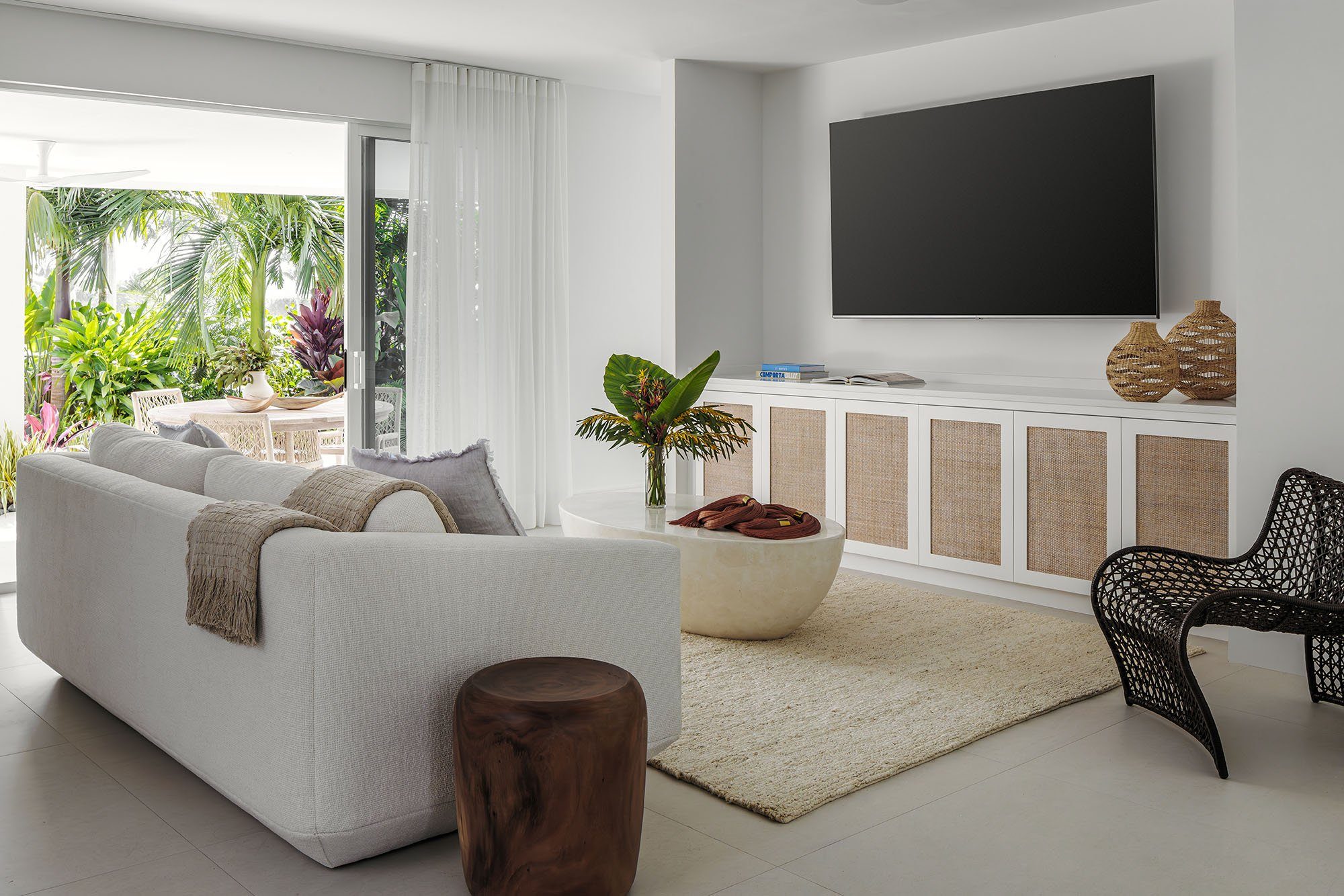 Serene living room with a linen sofa, woven cabinetry, and a tropical garden view in a Boca Raton home