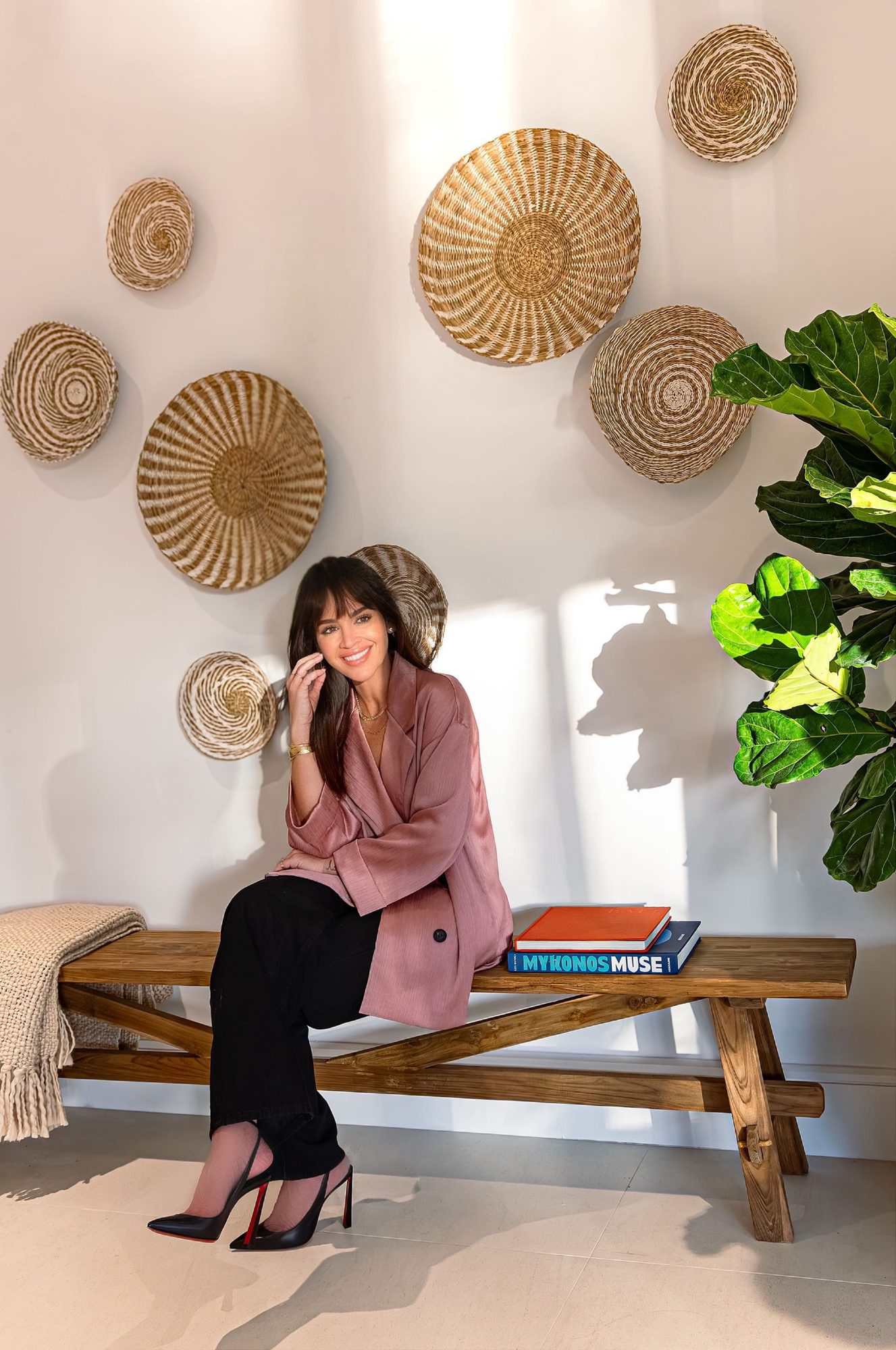 Raisa Imar Ortiz seated on a wooden bench before a wall of woven art